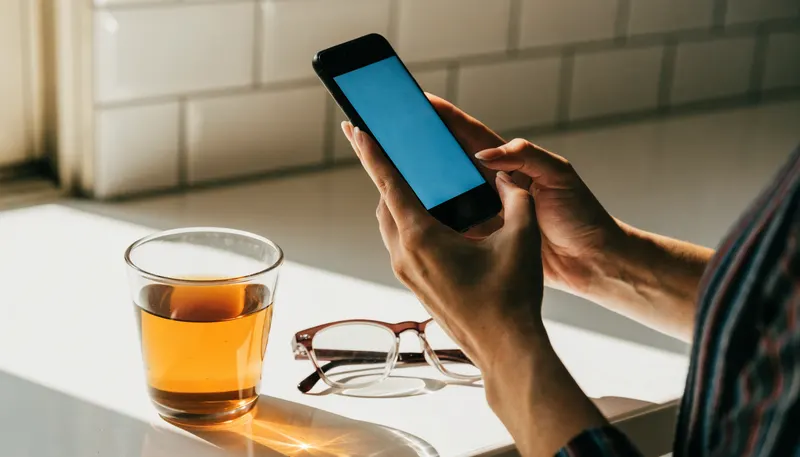 Hands holding a phone on a kitchen bench beside a cup of tea